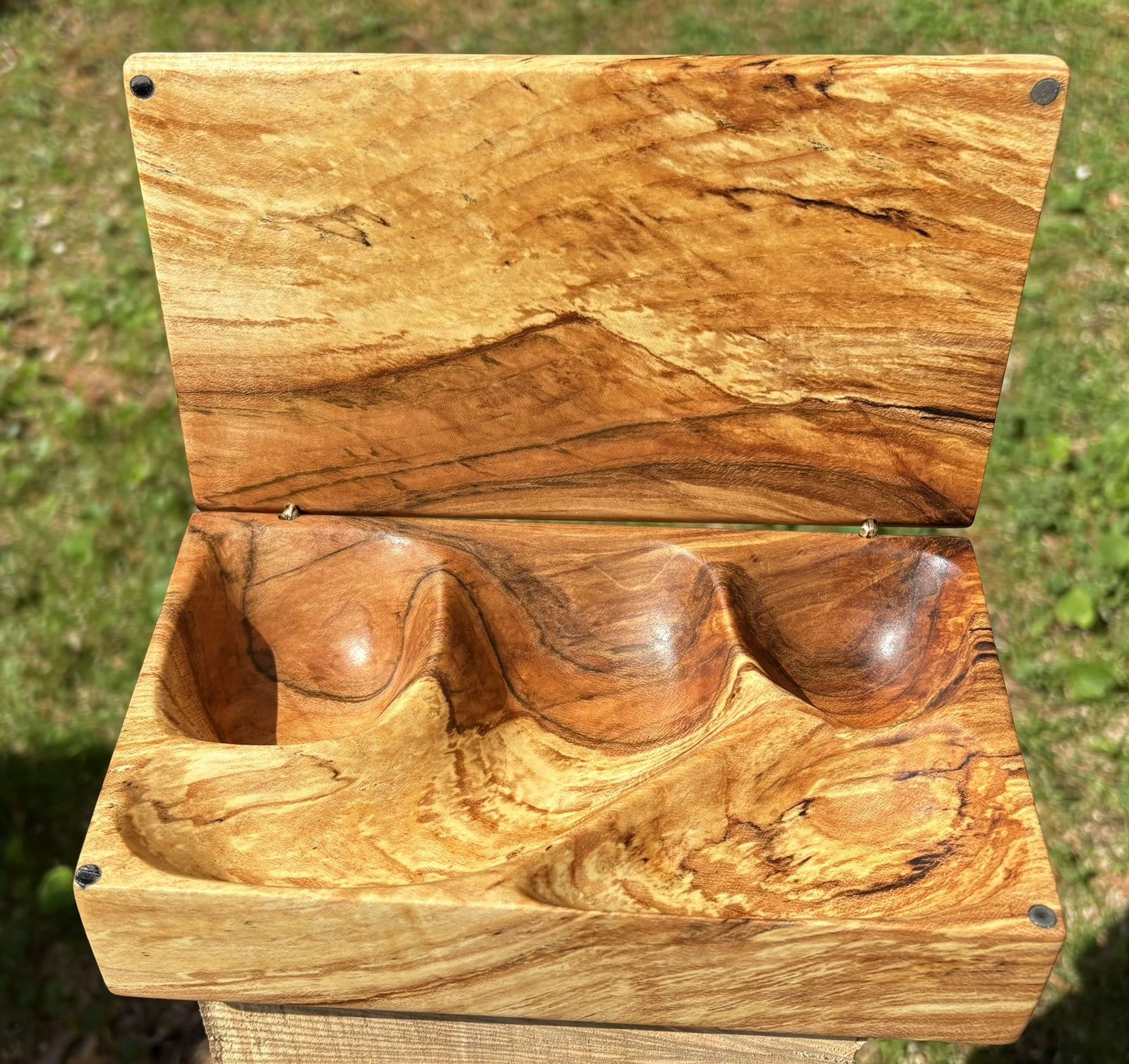 The box open, the underside of the lid showing the dark spalting mountains, the base hollowed into three carved wells for jewelry.